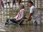 A man assists a person in a wheelchair through a waterlogged area after heavy rain, at BHU Hospital, in Varanasi on Tuesday. (PTI)