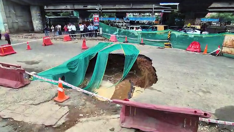 A major portion of the road caves in following an intense rainfall at IFFCO Chowk, in Gurugram on Tuesday. The spot is cordoned off and concerned officials present. (ANI Video Grab) A major portion of the road caves in following an intense rainfall at IFFCO Chowk, in Gurugram on Tuesday. The spot is cordoned off and concerned officials present. (ANI Video Grab)