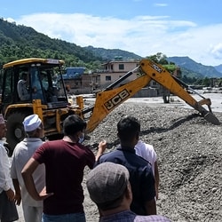 Residents gather along a road as workers use a bulldozer to clear mud and debris after flash floods in the Devighat area in Nepal's Nuwakot district.