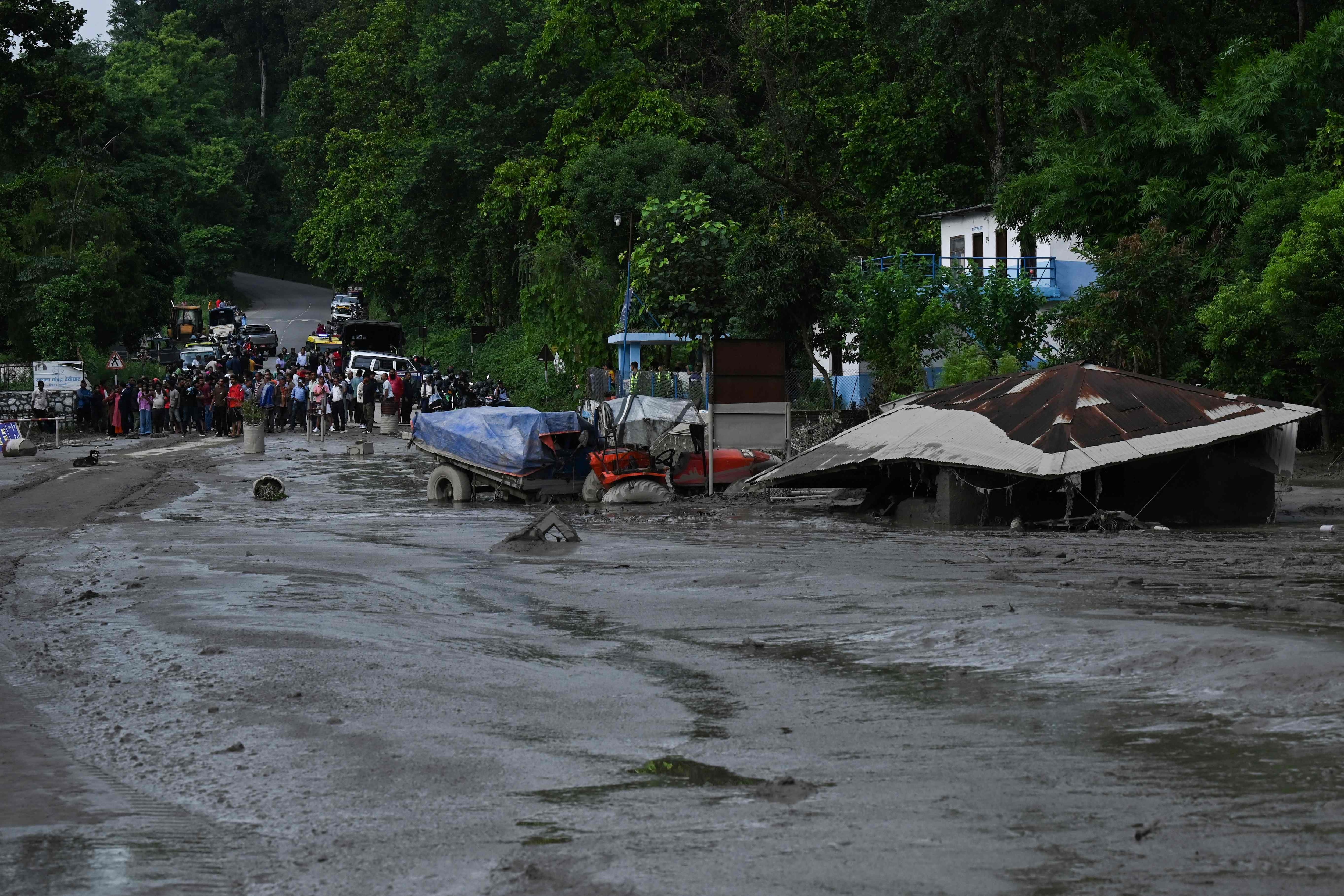 Residents look at buildings and street submerged by mud following flash floods and a landslide disaster in Devighat.