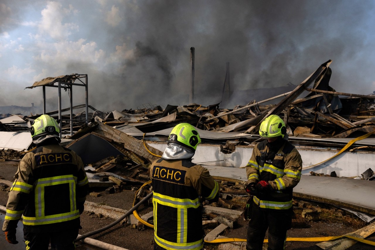 Firefighters stand next to debris after recent strikes in Kyiv.