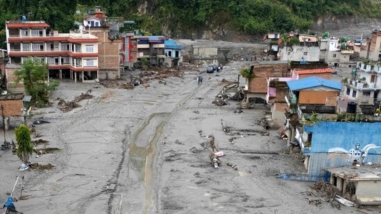 Aerial photograph showing people walking along a road in the middle of houses covered in sludge in the aftermath of flash floods at Devighat in Nepal's Nuwakot district.