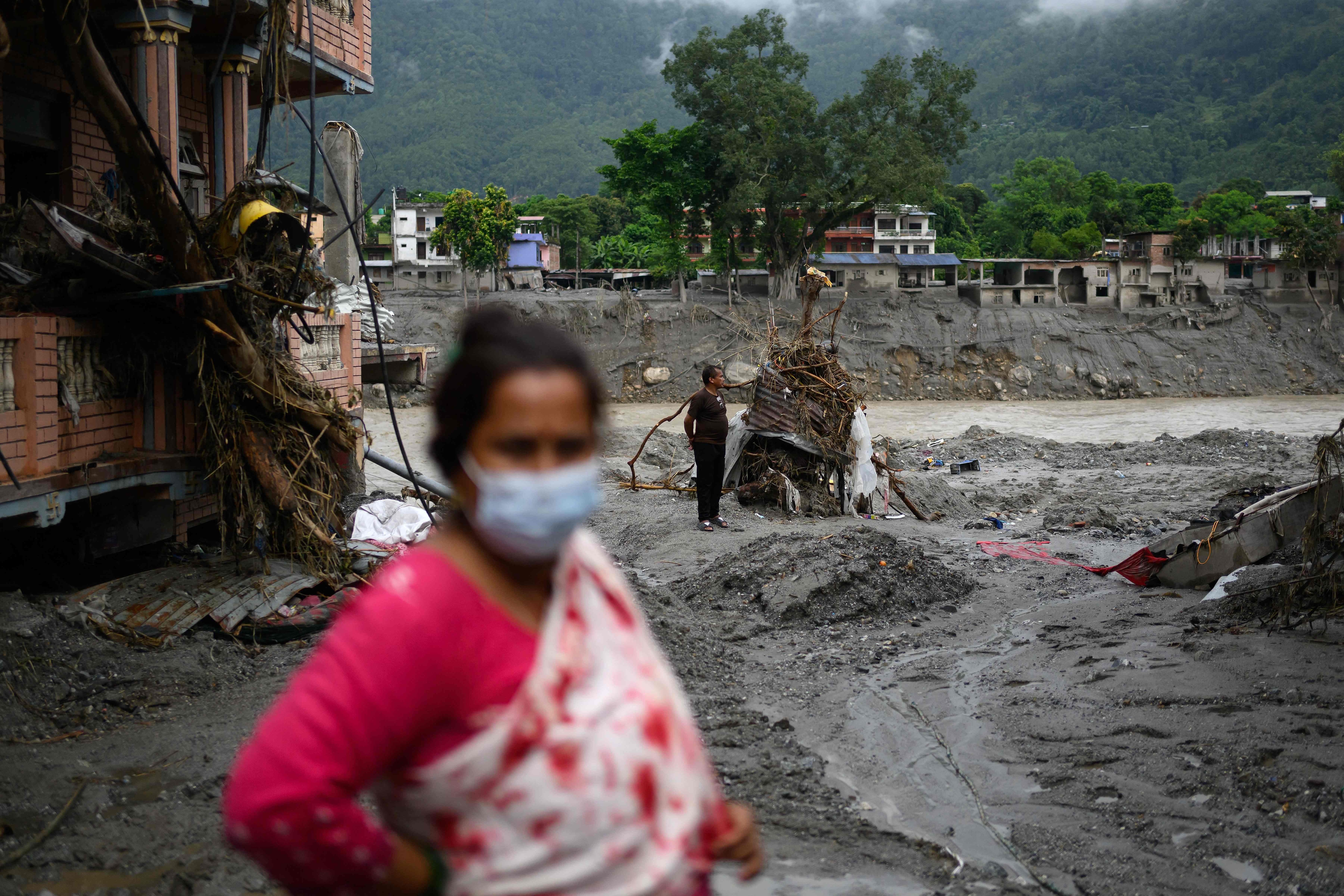 TOPSHOT - A man (R) stands amidst houses heavily covered in mud following flash floods at Devighat in Nepal's Nuwakot district on August 29, 2026. Rescuers in Nepal and China were still battling on August 29 to locate thousands of people missing days after a deadly, tsunami-like wall of water and debris swept through the Himalayan region, engulfing villages. Nearly 3,000 people were still missing on August 29 and 633 confirmed dead after flash floods and landslides hit the Nepal-Tibet border. (Photo by Manan VATSYAYANA / AFP) (AFP)