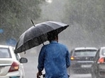 A man rides a bicycle with an umbrella in hand amid rainfall in Delhi.