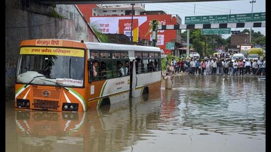 Passengers look out from inside a UPSRTC bus stranded at a waterlogged underpass following heavy rain, in Mirzapur, Tuesday. (PTI Photo)