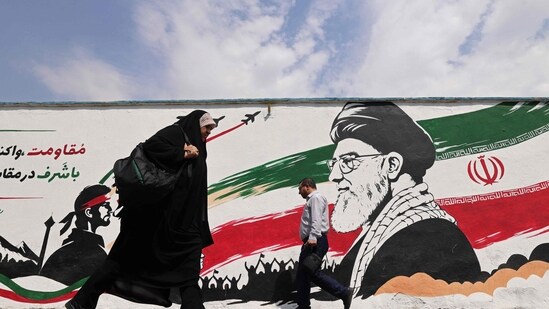 Pedestrians walk past a wall mural of Iran's slain supreme leader Ayatollah Ali Khamenei, along a street in downtown of Tehran on August 31.