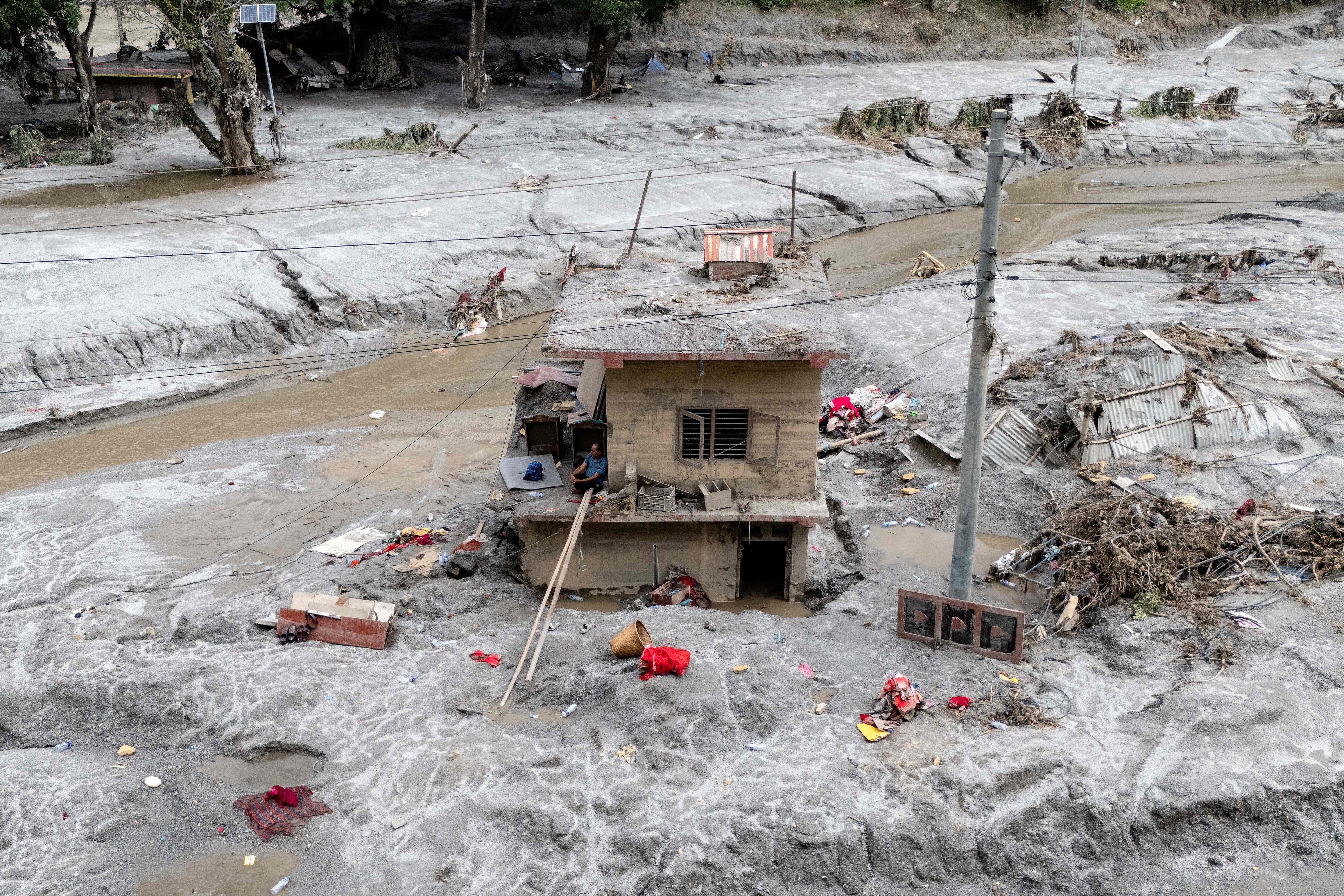 This aerial photograph shows Om Bahadur (C), sitting on the ledge of his damaged house, a week after the devastating flash floods at Baireni in Nepal's Dhading district on September 2, 2026. (AFP)