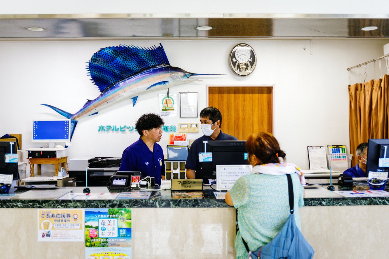 Keiichiro Tabata, who runs the Hotel Bigmarine Amami, at the reception desk. Keiichiro Tabata, who runs the Hotel Bigmarine Amami, at the reception desk.