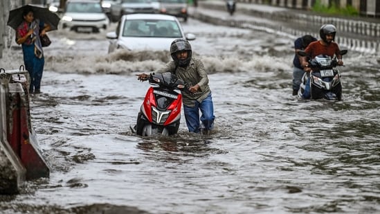 Commuters wade through a water logged stretch at Mayur Vihar Phase 2 near NH24 amid heavy rains in New Delhi.