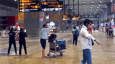 Passengers with their luggage walk through the waterlogging conditions at Indira Gandhi International Airport after heavy rainfall. (ANI Video Grab)