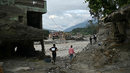 Residents walk past damaged houses covered in sludge in the aftermath of flash floods in Trishuli, (AFP)