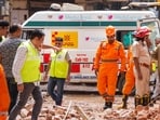 NDRF, fire services, and medical personnel move past an ambulance stationed near the site of the building collapse, at Satya Niketan, in New Delhi.