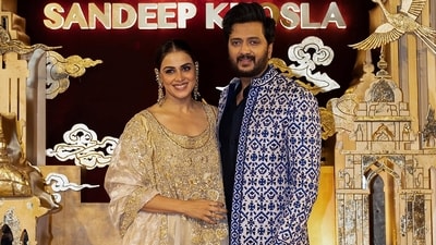 Genelia opted for a traditional gold and beige kurta set paired with heavy statement earrings, and a long gold hair accessory, while Riteish Deshmukh complemented her look by wearing a coordinated, dapper ethnic outfit. (abujanisandeepkhosla/Instagram) Genelia opted for a traditional gold and beige kurta set paired with heavy statement earrings, and a long gold hair accessory, while Riteish Deshmukh complemented her look by wearing a coordinated, dapper ethnic outfit. (abujanisandeepkhosla/Instagram)