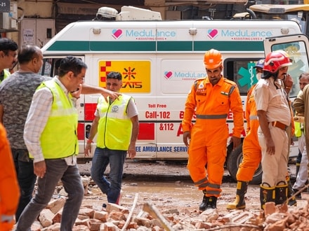 NDRF, fire services, and medical personnel move past an ambulance stationed near the site of the building collapse, at Satya Niketan, in New Delhi.