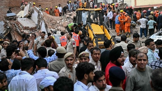 People gather to watch as rescue personnel conduct a search operation at the site following a building collapse in the Satya Niketan area in New Delhi