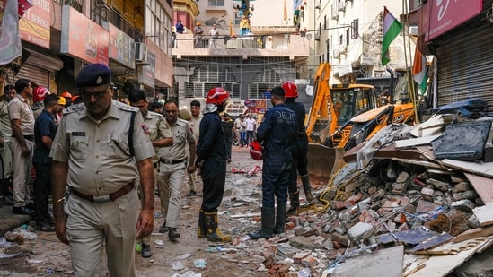 Rescue personnel stand near debris during a rescue operation on the second day after a 50-year-old five-storey building housing a boys' hostel collapsed in a congested bylane in Satya Niketan near Delhi University's south campus