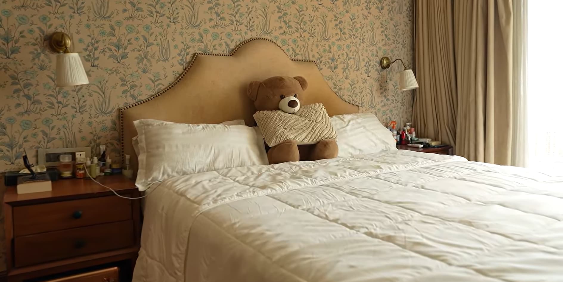 Her bedroom features a soft beige palette, a tufted headboard and floral wallpaper.