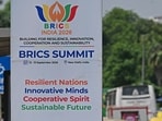 Pedestrians wait at a bus stand near a hoarding, displayed ahead of the BRICS summit in New Delhi on September 9, 2026. (Photo by Sajjad HUSSAIN / AFP)