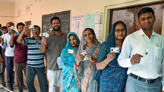 Voters stand in a queue and show their voter ID cards during the Municipal Corporation elections at a polling station, in Jaipur on Friday.

