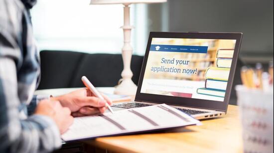 Young man writing college or university application form with pen and paper. Student applying or filling document. Scholarship, grant or admission. School website in laptop. (Getty Images/iStockphoto)