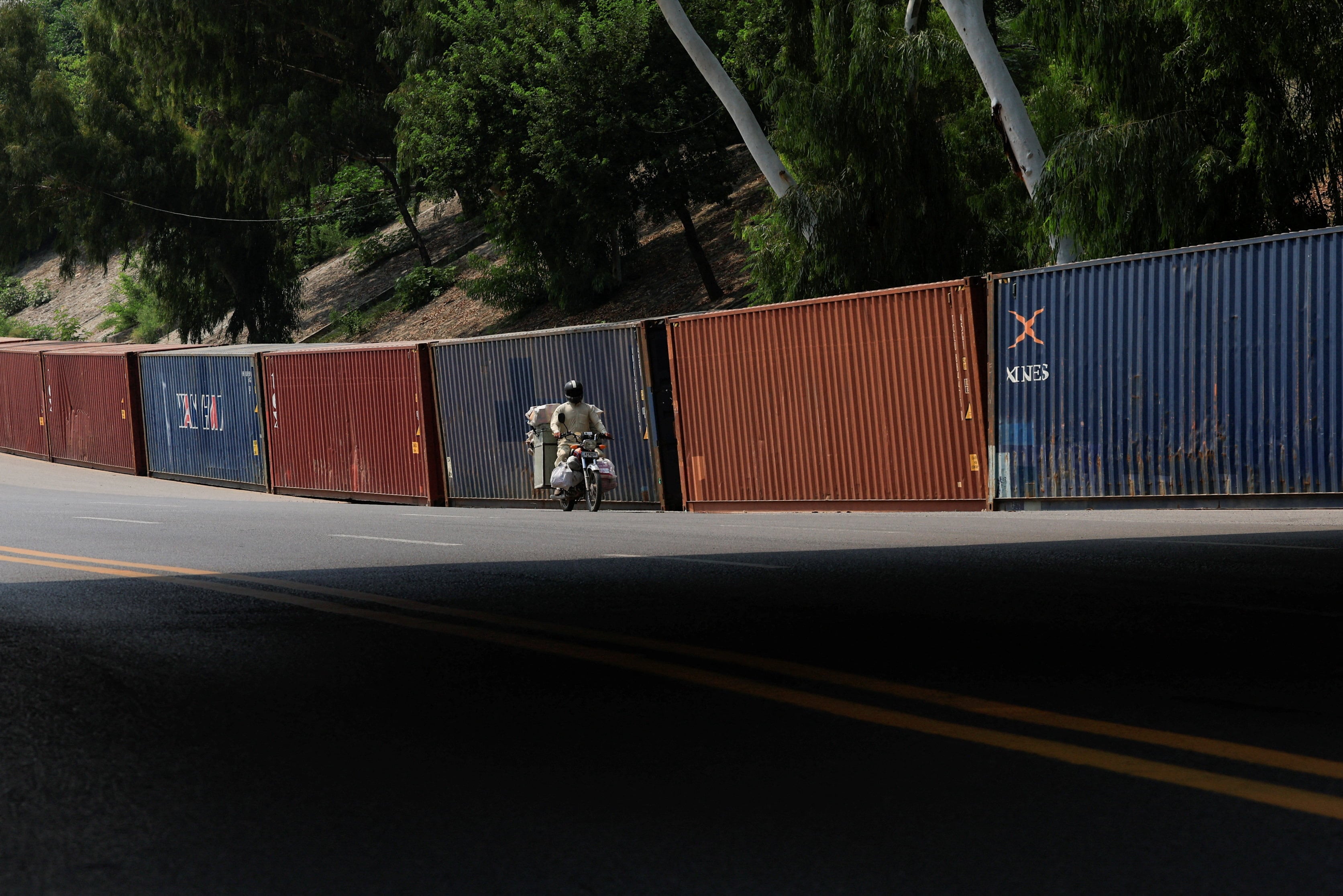 A man rides a motorcycle past shipping containers placed as a precaution to block the area ahead of a planned march by Imran Khan's party. (REUTERS)