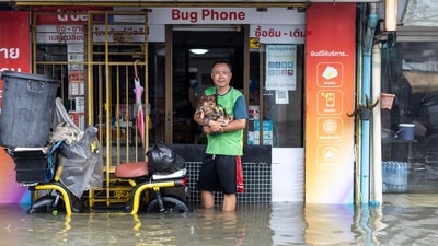 A man holding a small dog poses for a photo while standing in floodwaters in the Bang Bua district of Bangkok on September 26, 2026. (AFP)