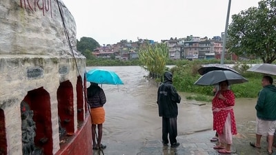 A view of local residents holding umbrellas and wearing raincoats as they watch the water level rise in the swollen Bagmati River following continuous downpours, in Kathmandu on Friday. (ANI Video Grab)