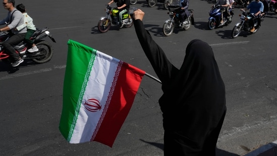 A woman chants slogan as she holds an Iranian flag while motorcyclists ride during a state-organized motorcycle parade called "Janfada," meaning "Sacrifice for Iran", in Tehran, Iran, Friday, Sept. 25, 2026.