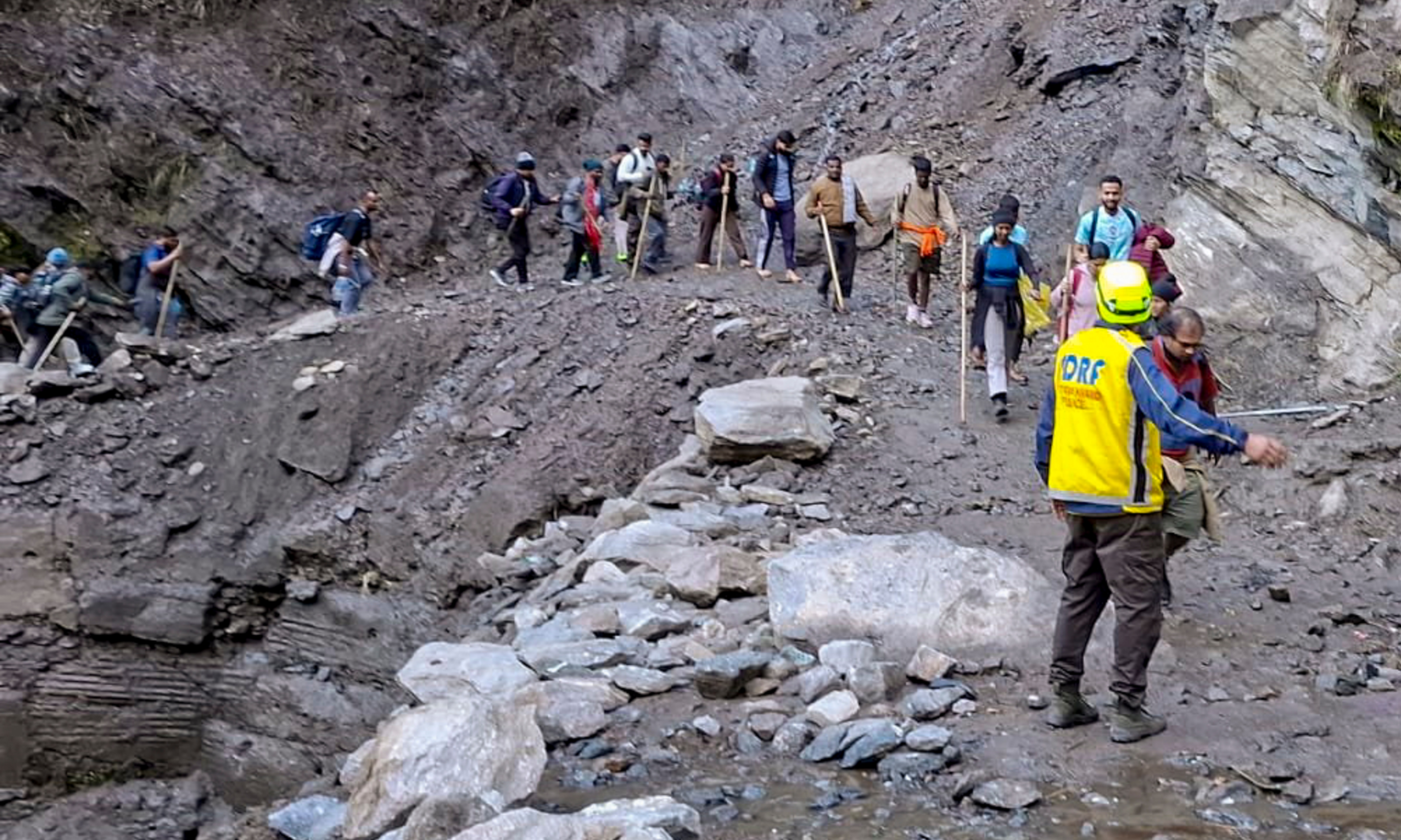 , Security and disaster response officer guides pilgrims through a damaged stretch of the trekking route near Chirbasa helipad on their way to Kedarnath Dham, in Rudraprayag district. (@RudraprayagPol/X via PTI Photo) (@RudraprayagPol) , Security and disaster response officer guides pilgrims through a damaged stretch of the trekking route near Chirbasa helipad on their way to Kedarnath Dham, in Rudraprayag district. (@RudraprayagPol/X via PTI Photo) (@RudraprayagPol)