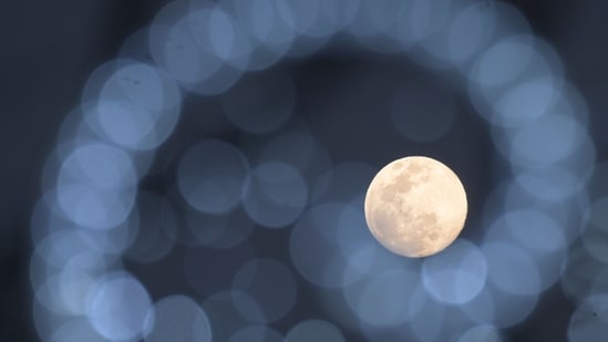 The Cold Moon is pictured behind Christmas decorations in Cali, Colombia on December 3, 2025. (Photo by JOAQUIN SARMIENTO / AFP)