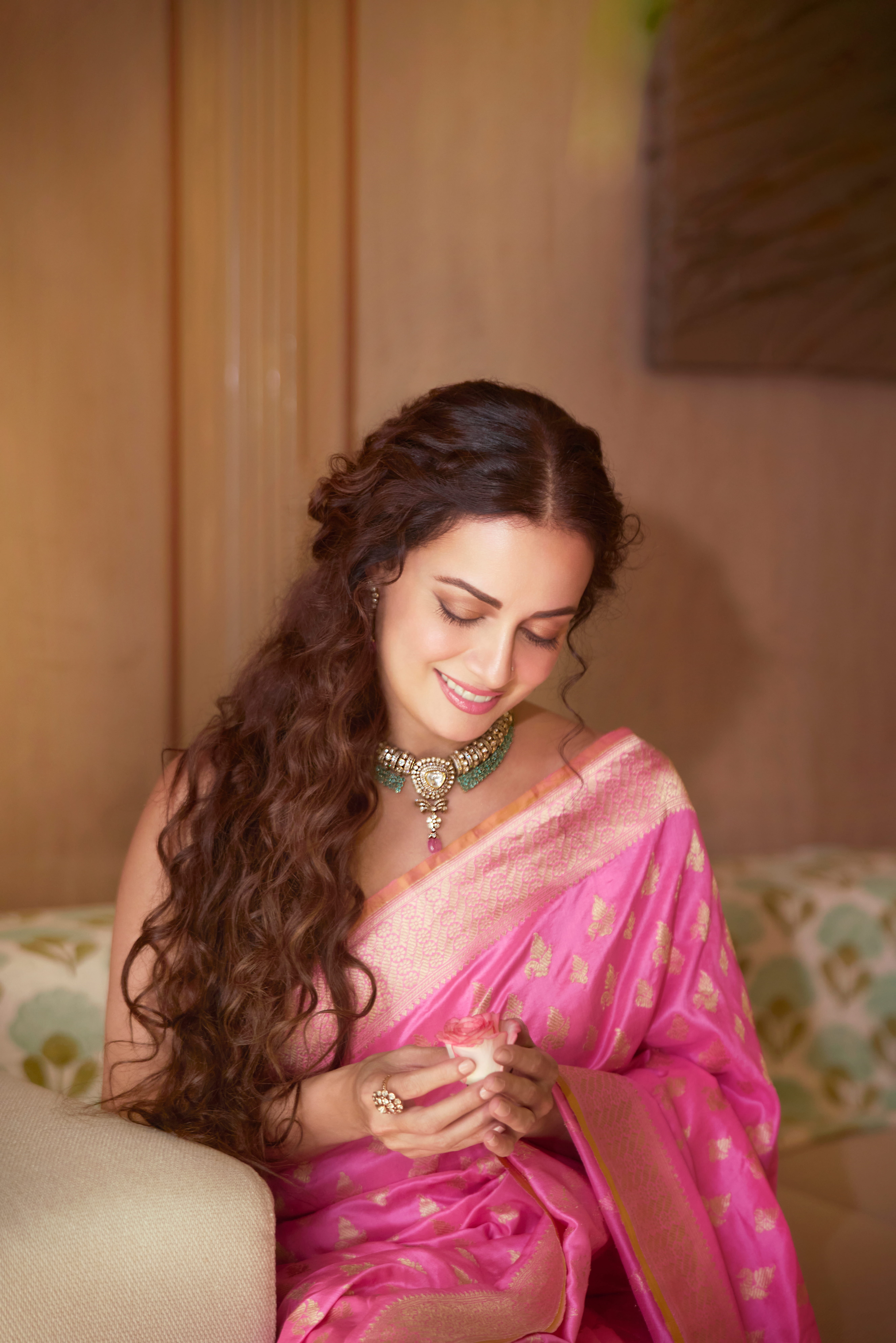 Dia is wearing a pink Banarasi Katan silk saree by Vidhi Singhania featuring leaf buti work and traditional konia corner motifs, paired with a statement necklace from Manubhai Jewellers.
