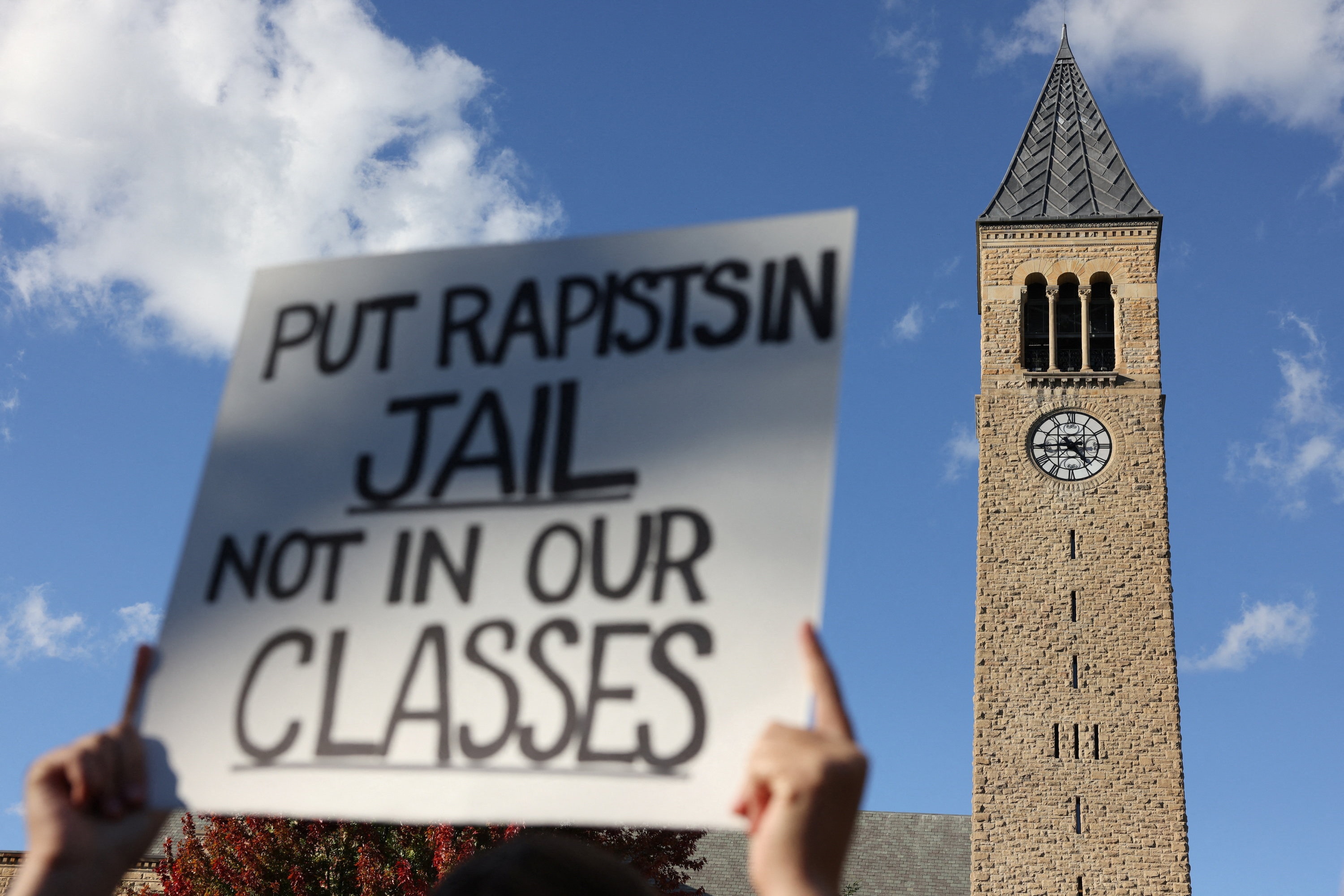 A demonstrator holds a placard as the McGraw Tower stands in the background during a Justice for Survivors rally at Cornell University in Ithaca, New York. (REUTERS)
