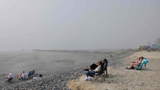 People sit (R) on what remains of an eroded beach as work continues on a sand replenishment project nearby along the Pacific Ocean shoreline in Oceanside, California. 