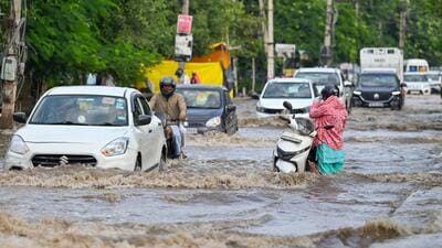 A woman stands next to a stalled two-wheeler on a waterlogged stretch in Sector 10, Gurugram, on Monday. (Parveen Kumar/HT Photo)