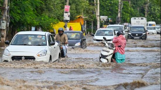 A woman stands next to a stalled two-wheeler on a waterlogged stretch in Sector 10, Gurugram, on Monday. (Parveen Kumar/HT Photo)