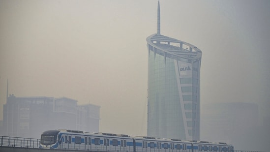 Gram it: A Metro train passes by a high-rise amid haze in Gurugram on Tuesday. In neighbouring Delhi, the AQI rose to 138 at 9.05am on TUesday, returning to the ‘moderate’ category after rain brought it down to 83, in the ‘satisfactory’ range, on Monday. (Photo: PTI)