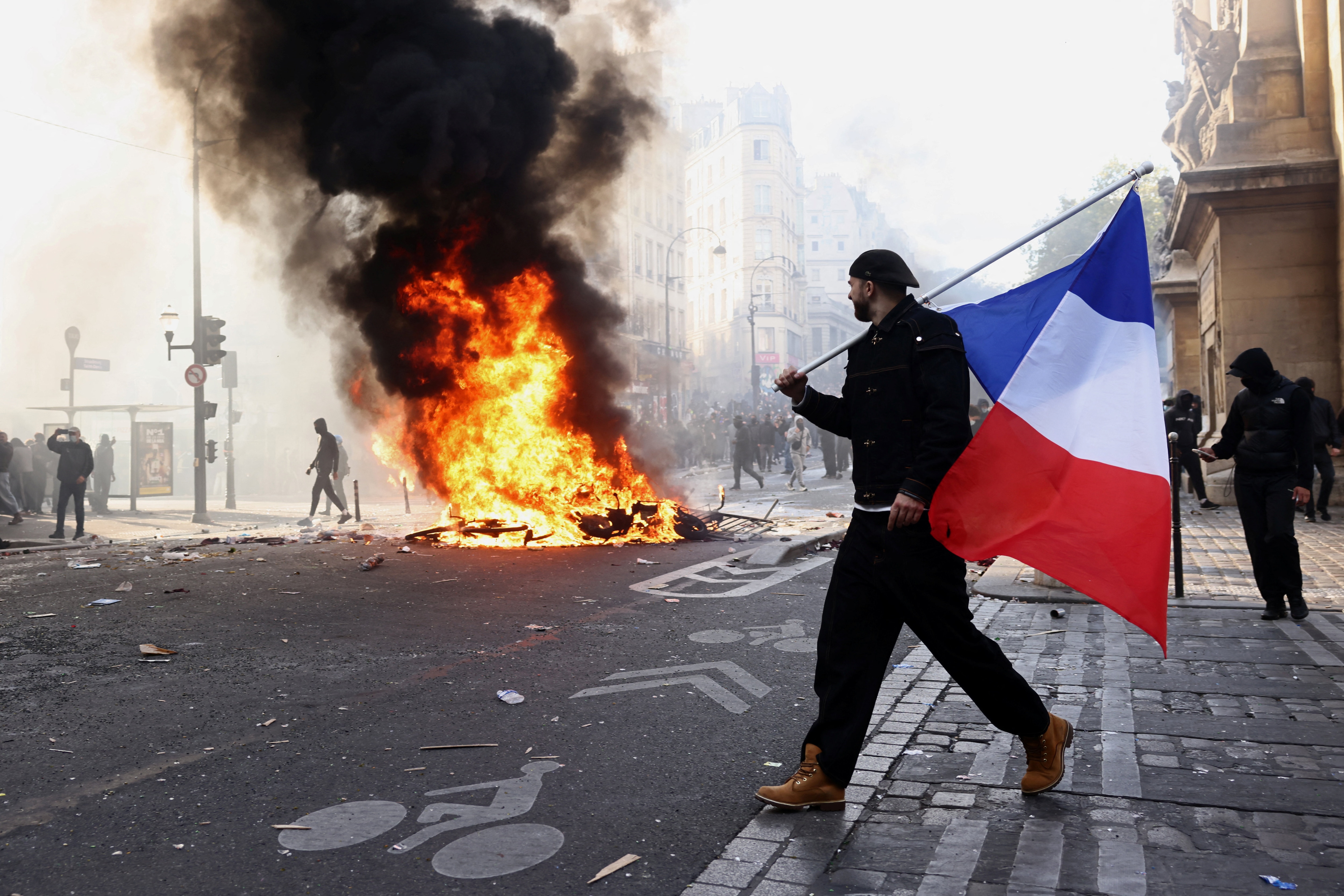 A protester holds a French flag next to burning objects amid clashes in a street near the Place de Republique during a day of demonstrations against the cost of living and rising fuel prices in Paris. (REUTERS)