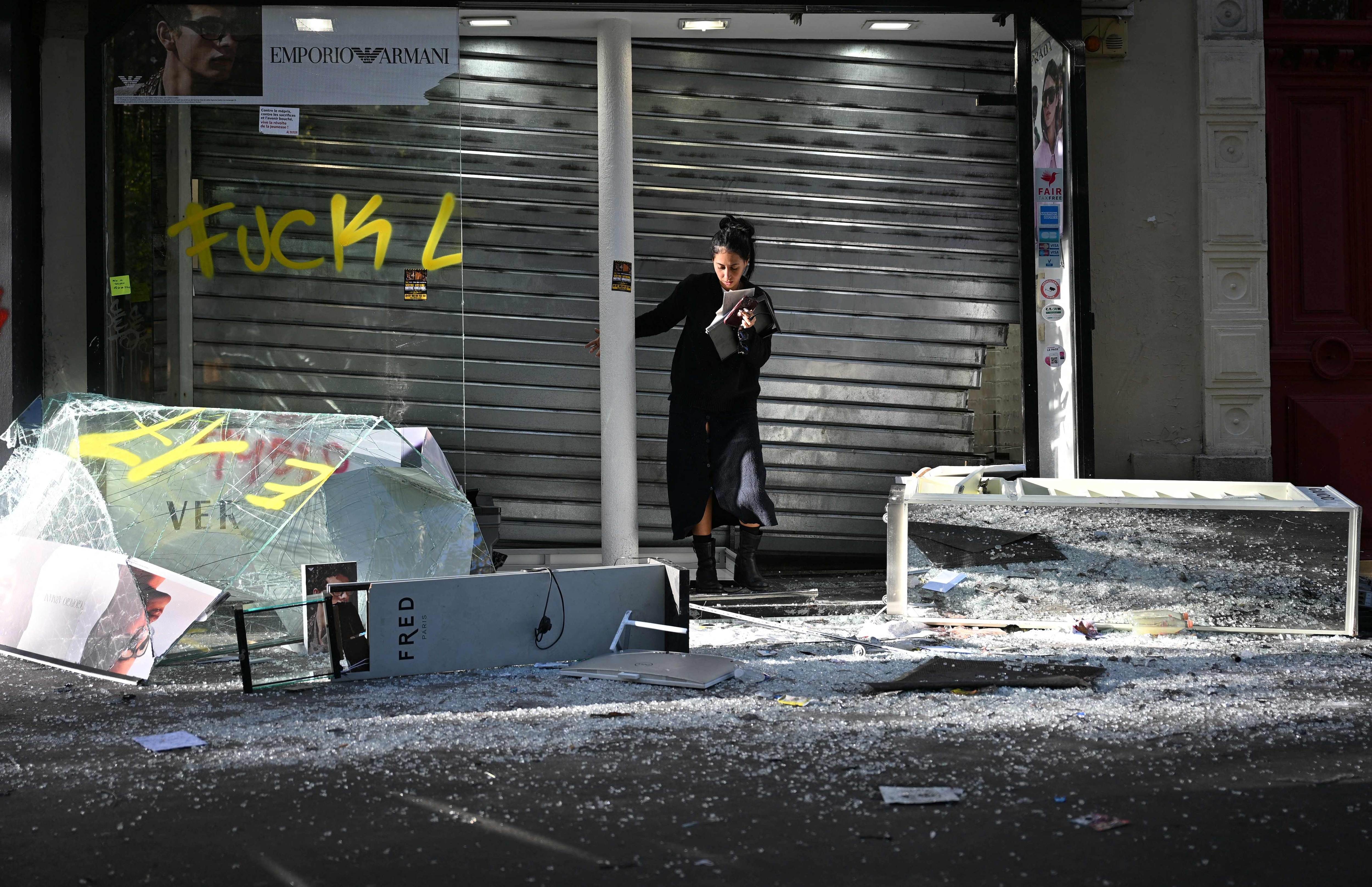 A shopkeeper clears up in front of her damaged shop in Paris on October 18, 2026, a day after nationwide protests against the "high cost of living". (AFP) A shopkeeper clears up in front of her damaged shop in Paris on October 18, 2026, a day after nationwide protests against the "high cost of living". (AFP)