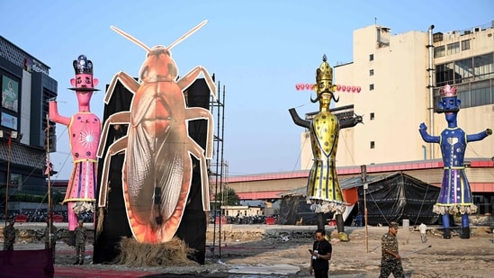 Security personnel stand guard beside an effigy of a cockroach.