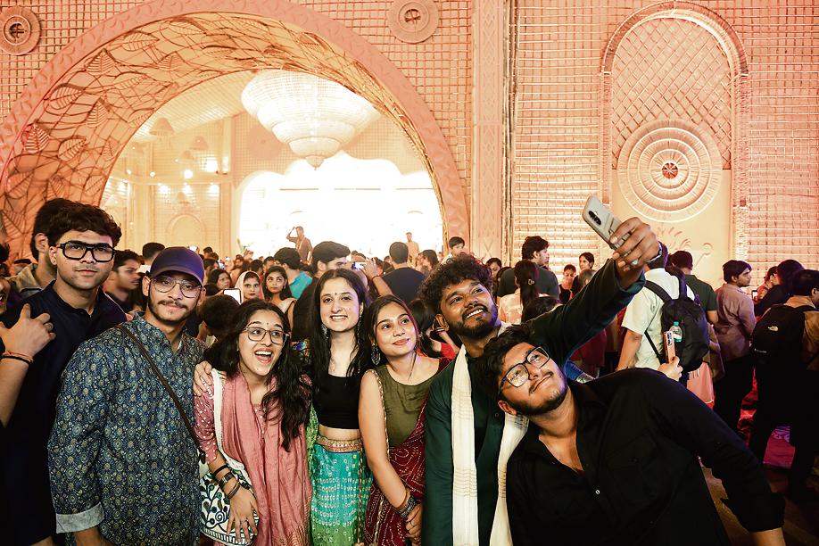A group of friends click selfies in front of the glowing pandal.