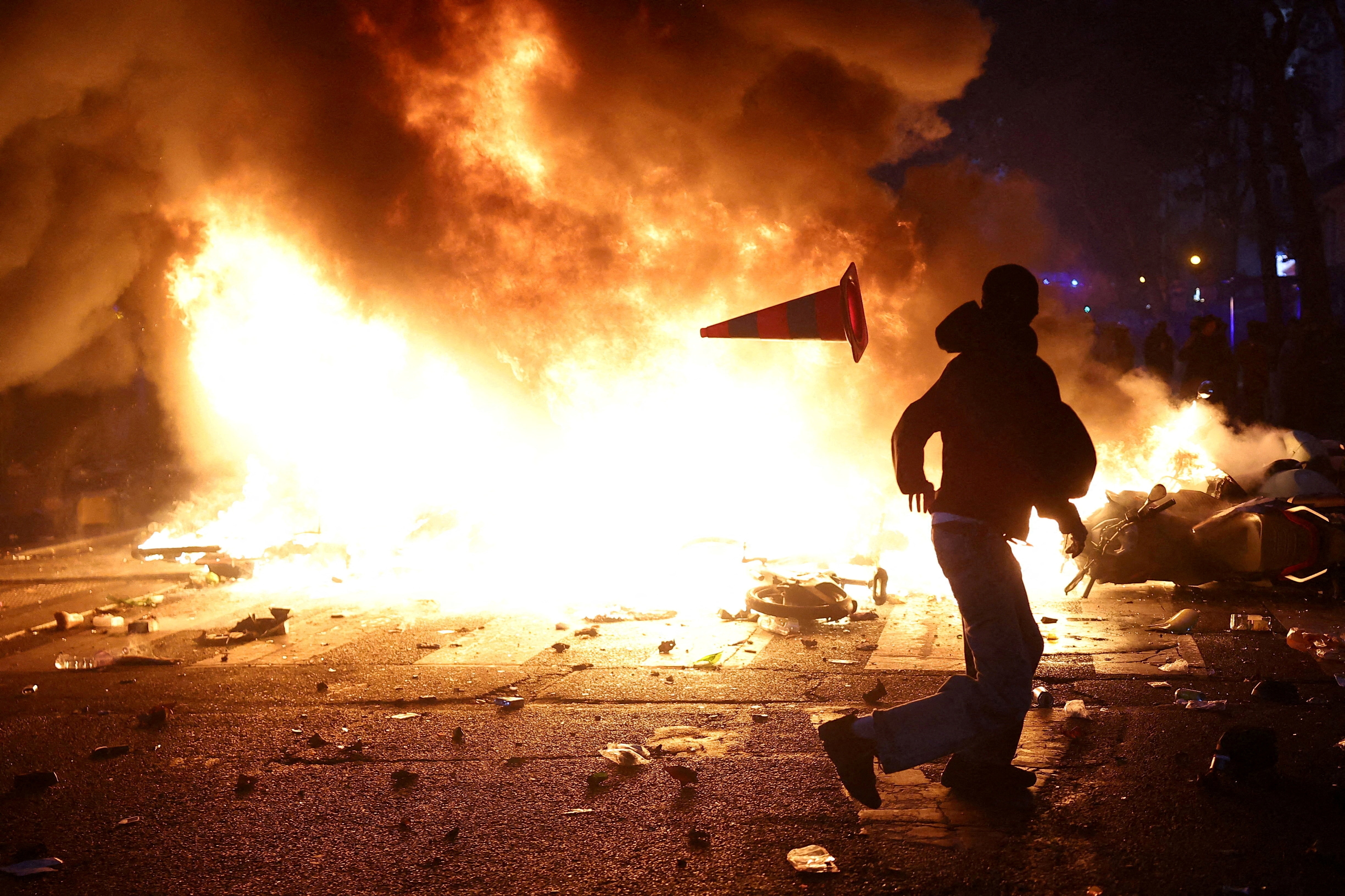 A man throws a plastic traffic cone through a burning barricade amid clashes during a day of demonstrations, in Paris. (Reuters)