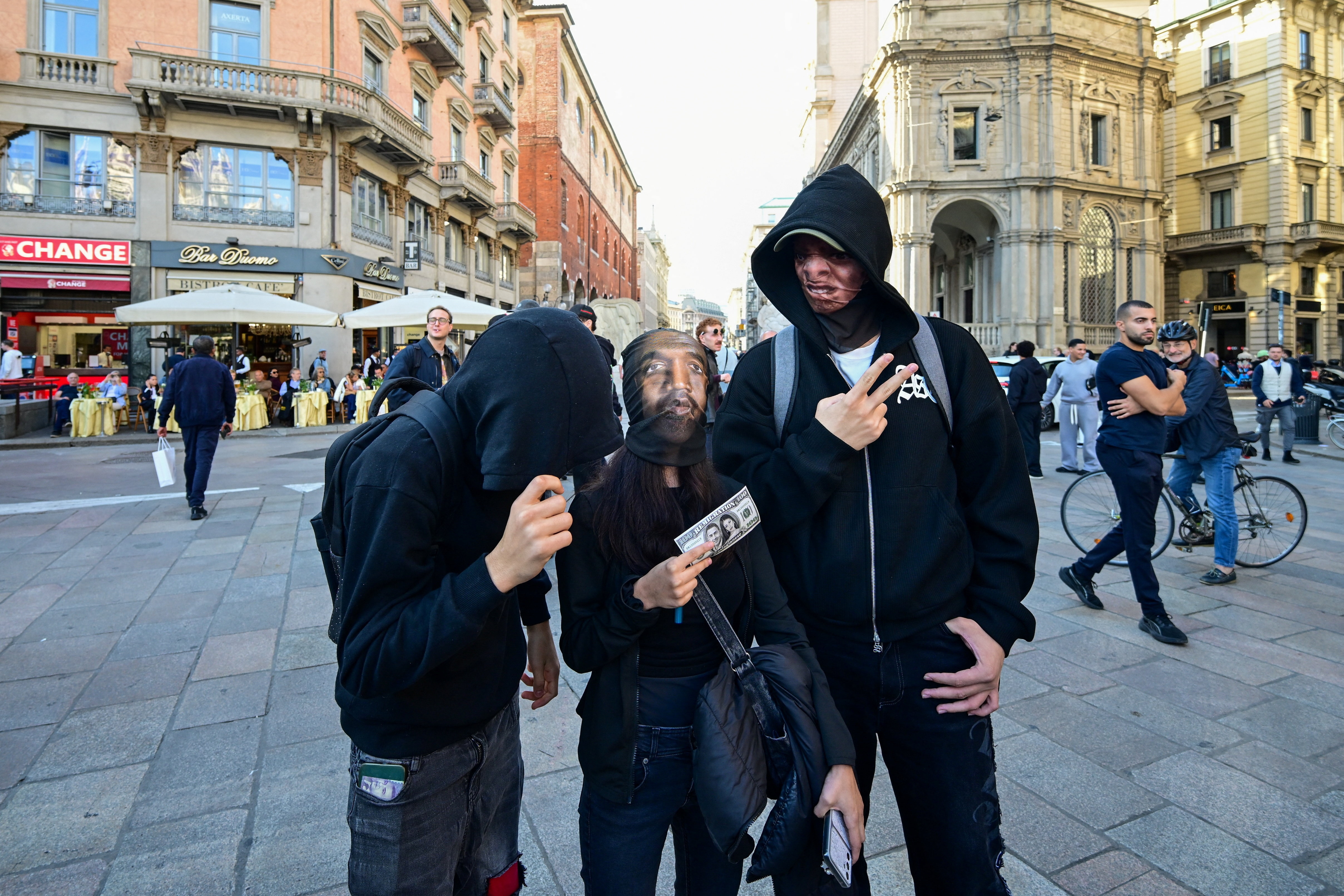 Three people, two wearing face coverings printed with portraits, pose for a photograph in central Milan, Italy, October 19, 2026. REUTERS/Daniele Mascolo (REUTERS)
