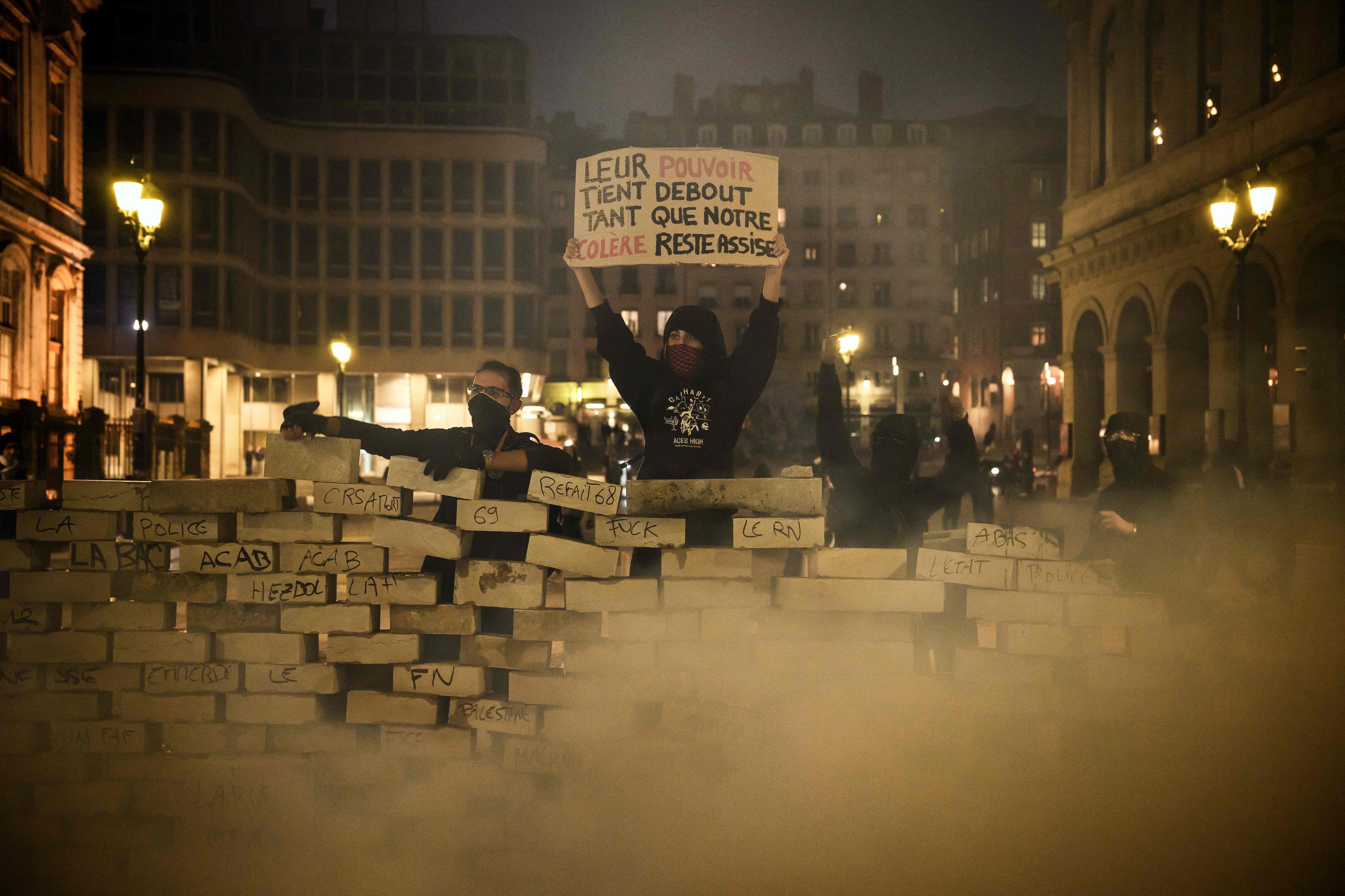 A demonstrator holds a placards which reads as "Their power stays standing as long as our anger stays seated" behind a barricade built with pavement stones, in Lyon. (AFP Photo) A demonstrator holds a placards which reads as "Their power stays standing as long as our anger stays seated" behind a barricade built with pavement stones, in Lyon. (AFP Photo)