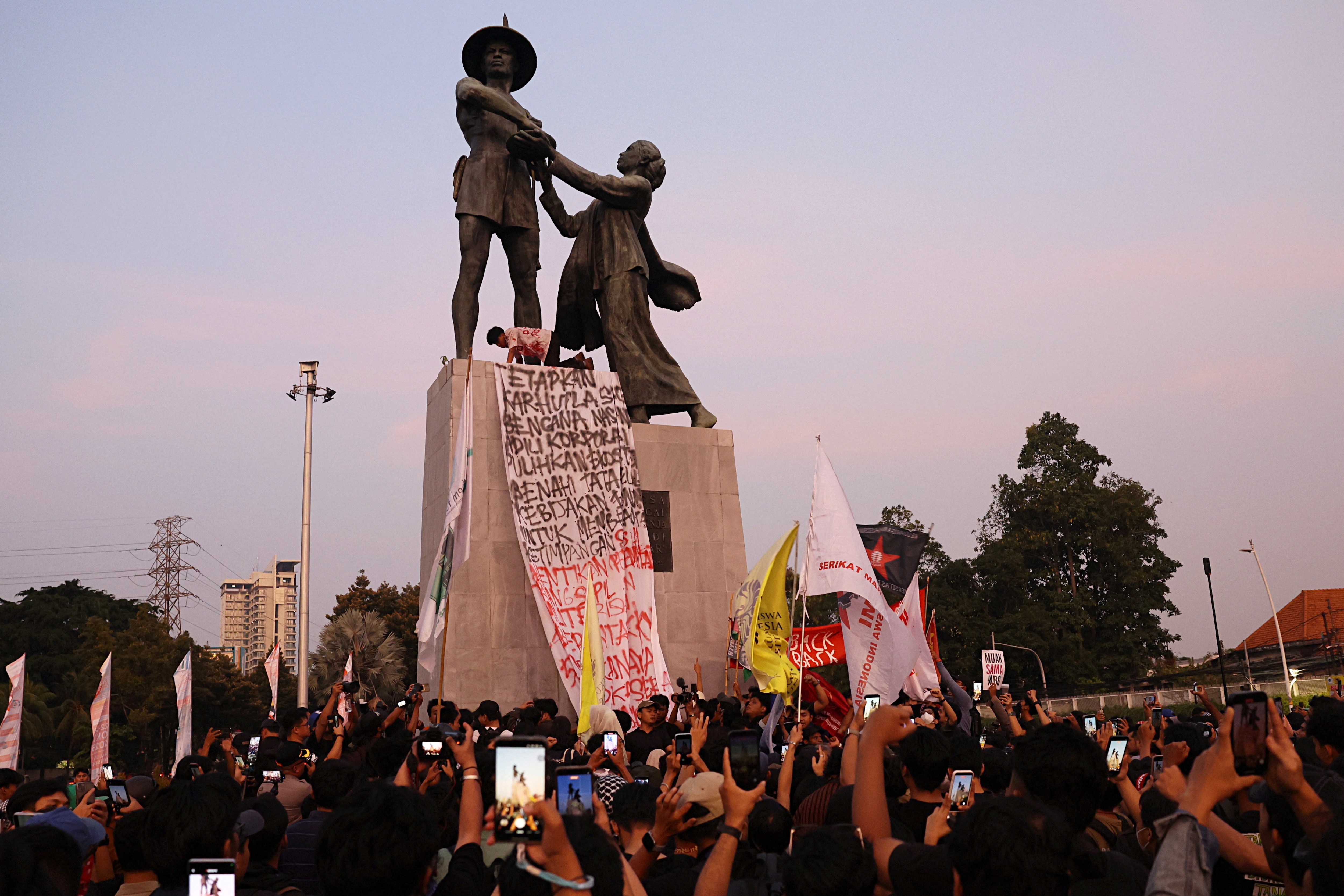 A protester hangs a banner on the Hero Monument, popularly known as Tugu Tani, during a demonstration against the government's handling of wildfires and calling for an end to corruption, collusion and nepotism. (REUTERS)