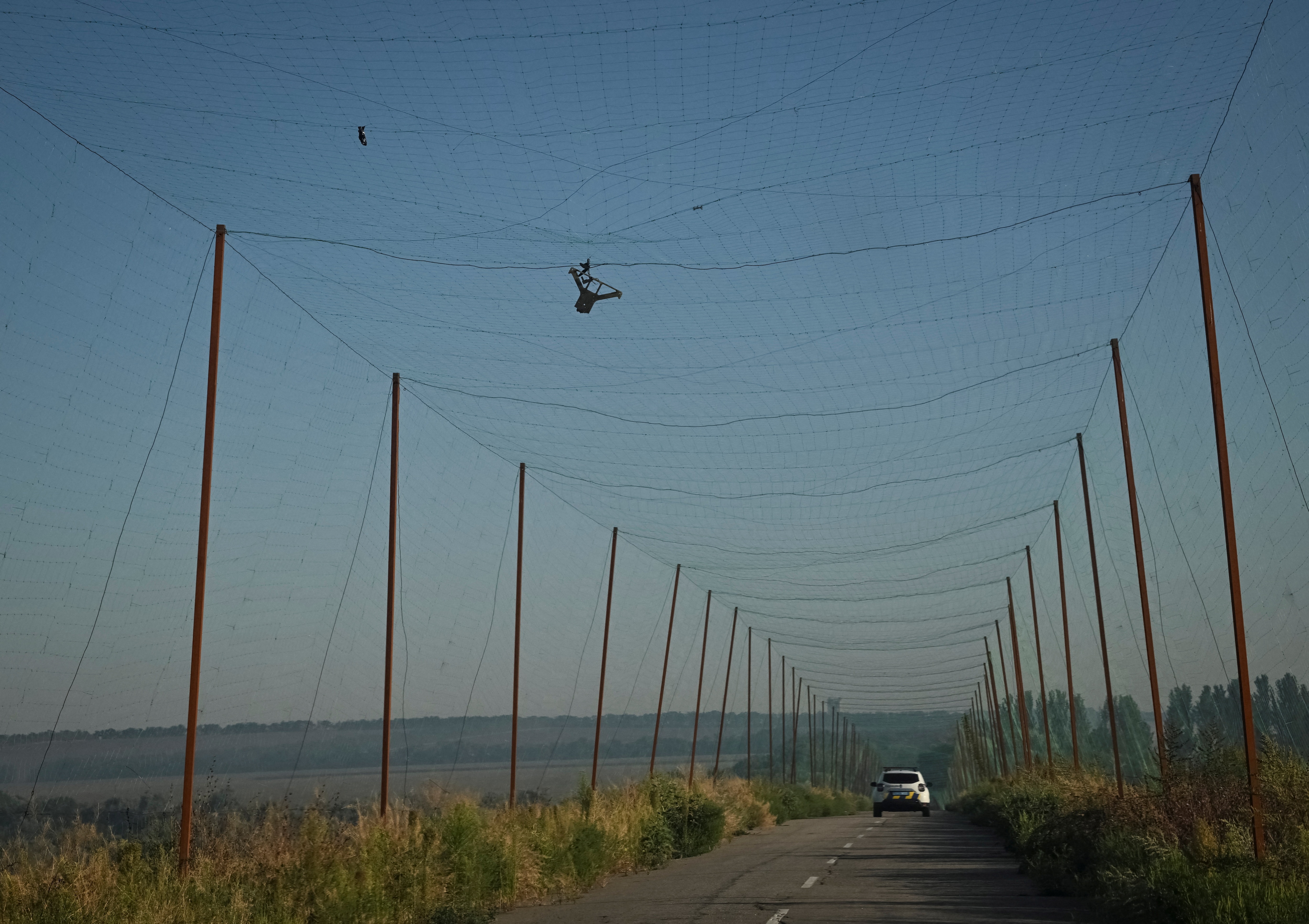 Members of the police evacuation unit drive along a road covered with an anti-drone net as a Russian FPV drone is stuck in it, in Zaporizhzhia region of Ukraine. (Reuters)