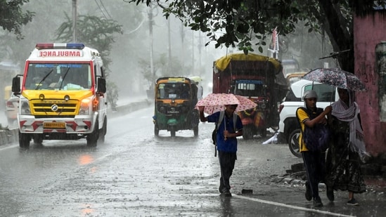 An ambulance and pedestrians holding umbrellas wade through a rain-slicked road amid heavy rainfall triggered by Cyclone Arnab, in Patna on Saturday. (ANI)