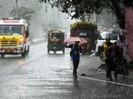 An ambulance and pedestrians holding umbrellas wade through a rain-slicked road amid heavy rainfall triggered by Cyclone Arnab, in Patna on Saturday.