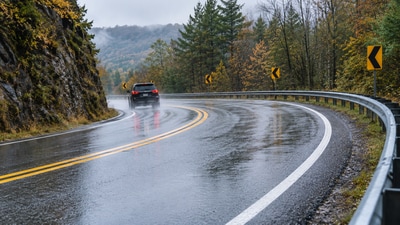 A representaive image of a wet, winding road illustrates the type of crash-prone curves where high-friction surface treatments can improve tire grip and reduce wet-road crashes. (AI- generated/ ChatGPT) A representaive image of a wet, winding road illustrates the type of crash-prone curves where high-friction surface treatments can improve tire grip and reduce wet-road crashes. (AI- generated/ ChatGPT)