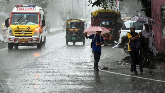 An ambulance and pedestrians holding umbrellas wade through a rain-slicked road amid heavy rainfall triggered by Cyclone Arnab, in Patna on Saturday.