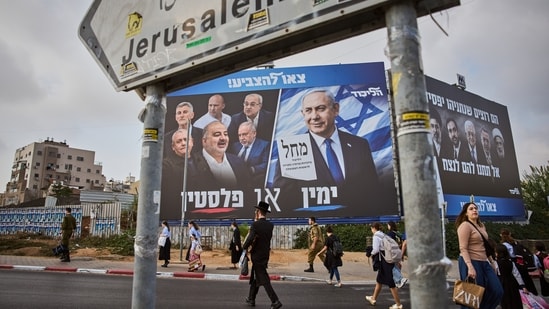 People walk past a Likud party campaign billboard featuring Israeli Prime Minister Benjamin Netanyahu alongside opposition party leaders and bearing the Hebrew slogan "Right or Palestine," ahead of Israel's general election, in Beni Brak, Israel,